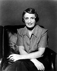 Half-length monochrome portrait photo of Ayn Rand, seated, holding a cigarette